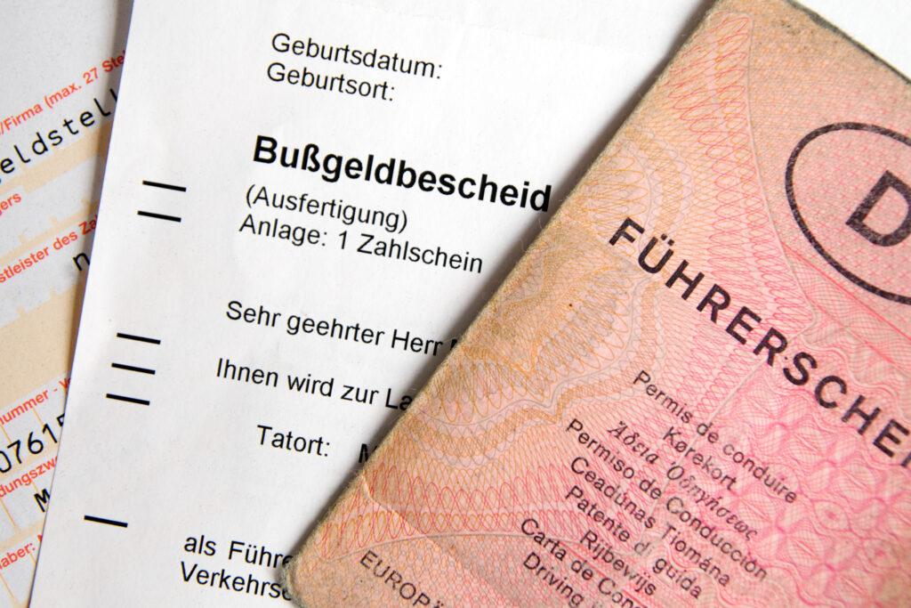 Close-up of a German Bußgeldbescheid fine notice overlapped by a pink euro banknote on the right side.